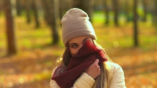 Young Attractive Girl in Autumn Park. He Looks at the Camera and Smiles, Touches the Scarf