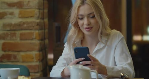 Attractive Woman Using Smartphone Drinking Coffee in Cafe