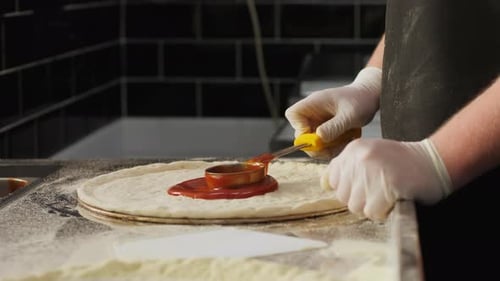 Chef Spreading Tomato Sauce on Pizza Dough