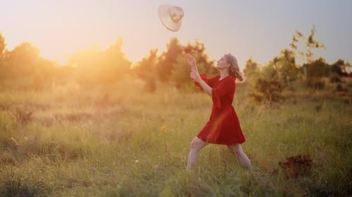 Woman in Red Dress with Hat in Field at Sunset