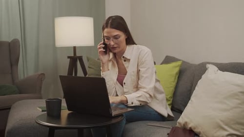 Calm European Woman Works at Home at the Computer and Talks on the Phone