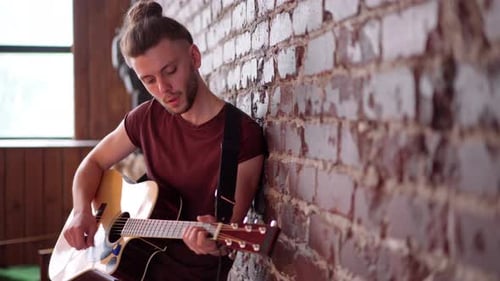 Man Plays Guitar, Leaning Against Brick Wall