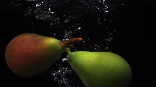 Two Pears Falls Into the Water with Splashes and Bubbles in Slow Motion.