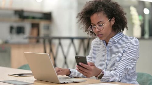 Hardworking African Businesswoman Using Smartphone and Laptop in Office