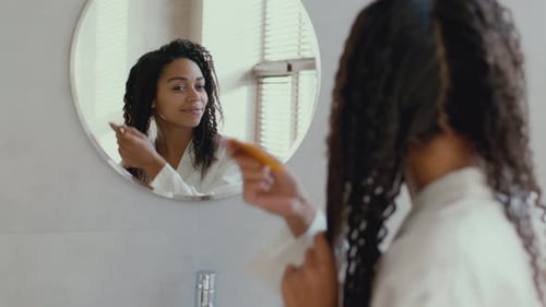 Woman Brushing Curly Hair in Bathroom Mirror