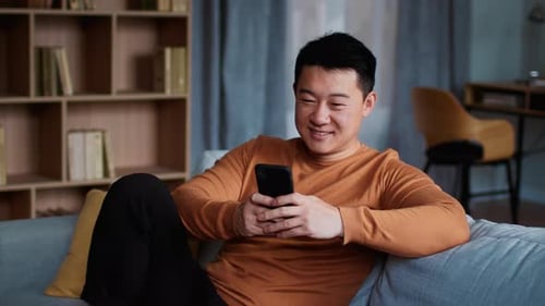 Smiling Man Relaxing at Home with Smartphone