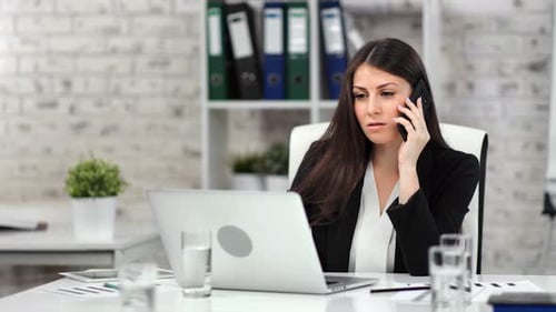 Businesswoman Working at Desk Talking on Cellphone