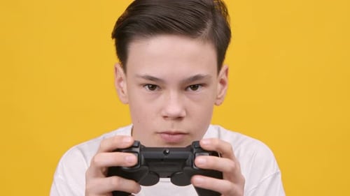 Focused Teen Boy Playing Video Game Over Yellow Studio Background