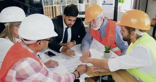 Un equipo de ingenieros masculino y femenino con un ingeniero jefe barbudo celebra una reunión sobre la construcción del futuro