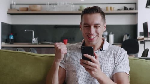 Man looks at phone, reacts with happiness