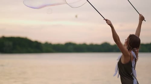 Woman Making Giant Bubbles by Lake at Sunset