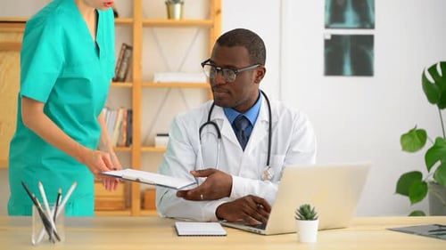 Young Male Doctor Working with Laptop Then Talking to Woman Nurse at Table in Hospital Spbas