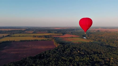 A beautiful red balloon flies in the evening over the river and the city.