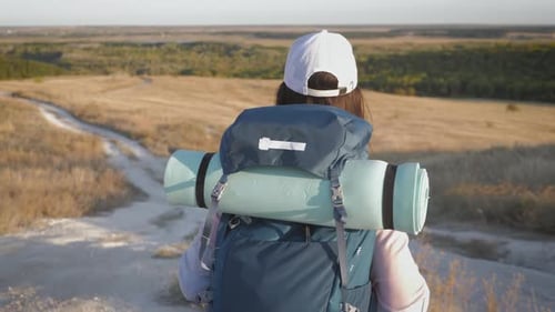 Woman with Backpack Walking in Rural Landscape