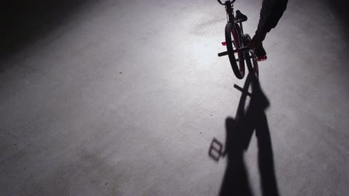 BMX rider doing tricks in dark warehouse.