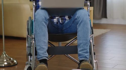 Man Using Laptop While Sitting in Wheelchair Indoors