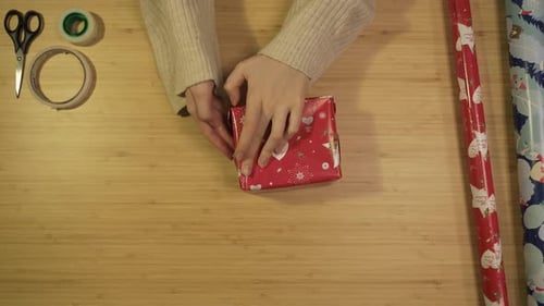 Hands Wrapping Christmas Present on Wooden Surface