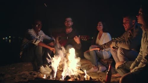 Friends Singing Around a Beach Campfire at Night