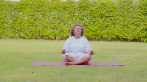 Senior Woman Meditating in Green Field