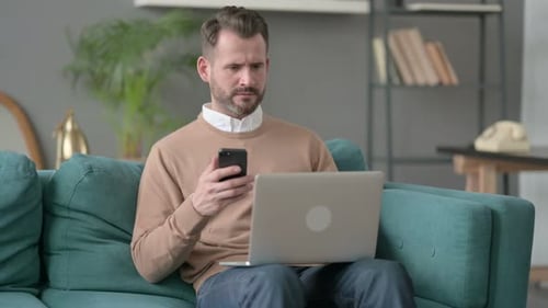 Man Relaxing on Couch Using Laptop and Smartphone