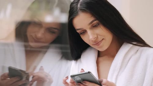 Woman in Robe Using Phone by Window