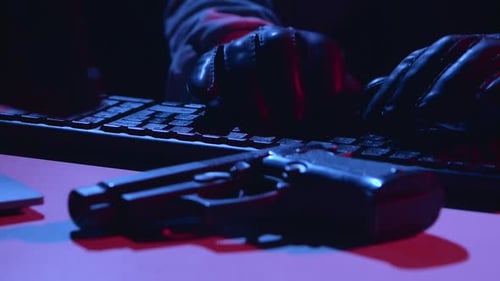 Man Types the Virus Data, on the Table There Is a Pistol. Close Up