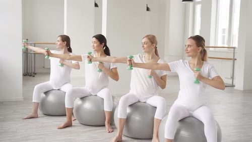 Pregnant Women Exercising with Dumbbells in Fitness Studio