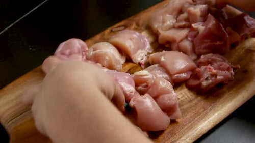 Woman's hands cut fresh chicken pieces on a wooden board close up