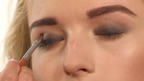 Make-up Artist Applying Bright Base Color Eyeshadow on Model's Eye and Holding a Shell with