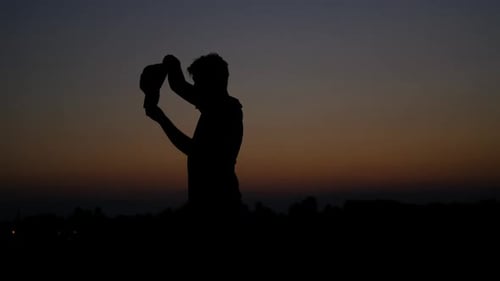 Silhouette Figure Adjusting Cap in Sunset