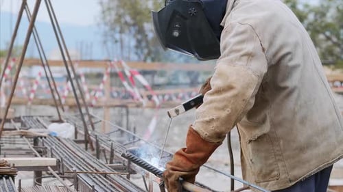 Schweißer auf der Baustelle schweißt Rohr mit Elektrode im Helm.
