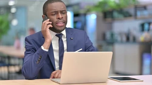 African Businessman with Laptop Talking on Phone in Office