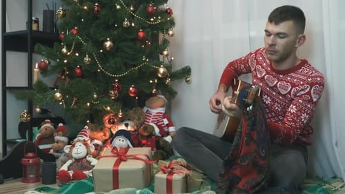 Man Plays Guitar by the Christmas Tree