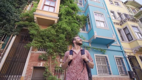 Man with Backpack Stands in Front of Colorful Buildings