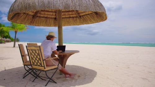 Erfolgreiche Geschäftsfrau mit gelbem Hut arbeitet am Laptop am Meer