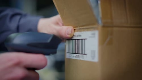 Closeup Male Hand Scanning Shipment Barcode on Cardboard Box in Terminal Warehouse