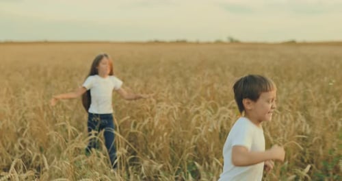 Beautiful Girl with Long Hair and a Boy are Running Along a Wheat Field