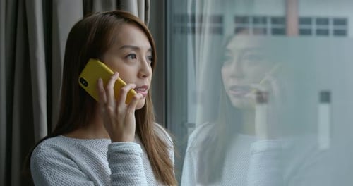 Woman chat on cellphone and stand beside the window