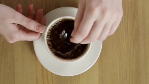 Woman Stirring Cup of Coffee on Wooden Table
