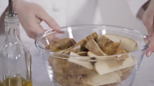 Step by step. Soaking potato wedges in a bowl of water to prepare baked potato wedges with spices.
