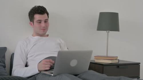 Young man video calling on laptop in bedroom