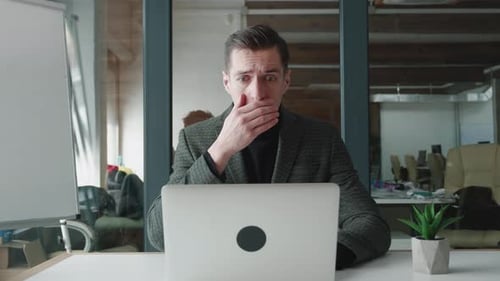 Gestresster Geschäftsmann ist schockiert, als er im Büro am Laptop arbeitet