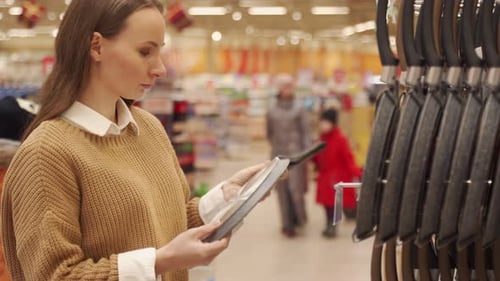 Young Woman in the Store Chooses a Frying Pan