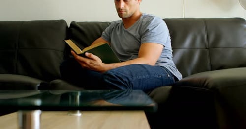 Man Reads Book on Sofa at Home