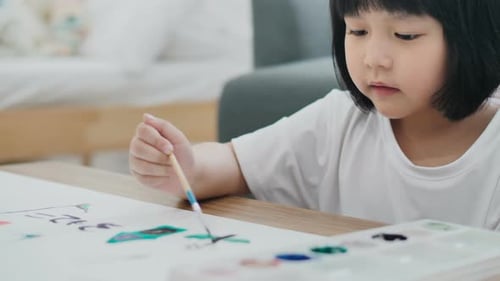 Happy Asian girl drawing picture with water color on paper.
