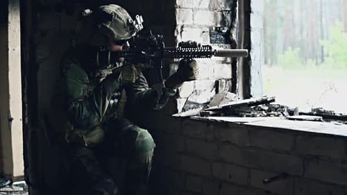 Soldat in Tarnung mit einer militärischen Waffe zielt durch das Gewehrvisier durch das Fenster eines