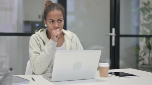 African Woman Coughing While Using Laptop in Office