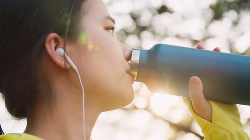 Close up of Asian sportswoman drinking from a water bottle after running at the street in urban.