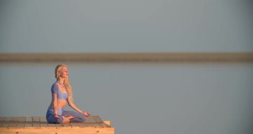 Frau sitzt auf dem Holzsteg des Sees und meditiert bei Sonnenuntergang