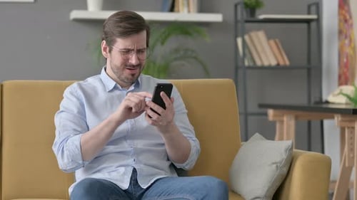 Young Man Having Loss on Smartphone at Home